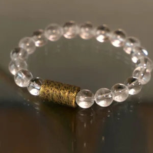 Close-up of healing crystal bracelet showing polished clear quartz beads and hammered brass spacer on wooden surface