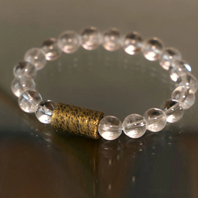 Close-up of healing crystal bracelet showing polished clear quartz beads and hammered brass spacer on wooden surface
