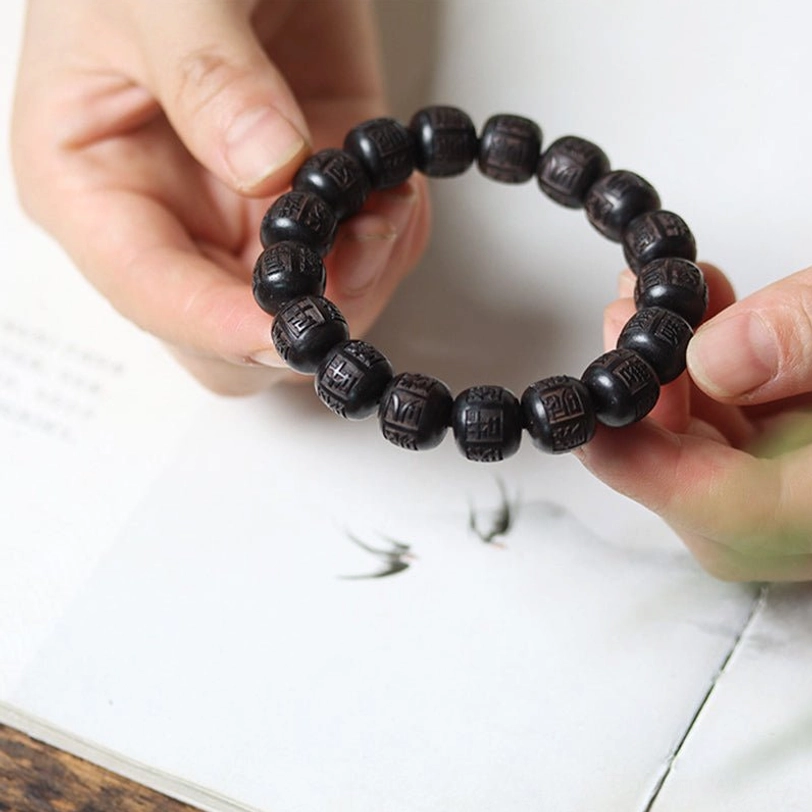 Ebony wood prayer bracelet held overhead on book showing complete strand with carved mantras