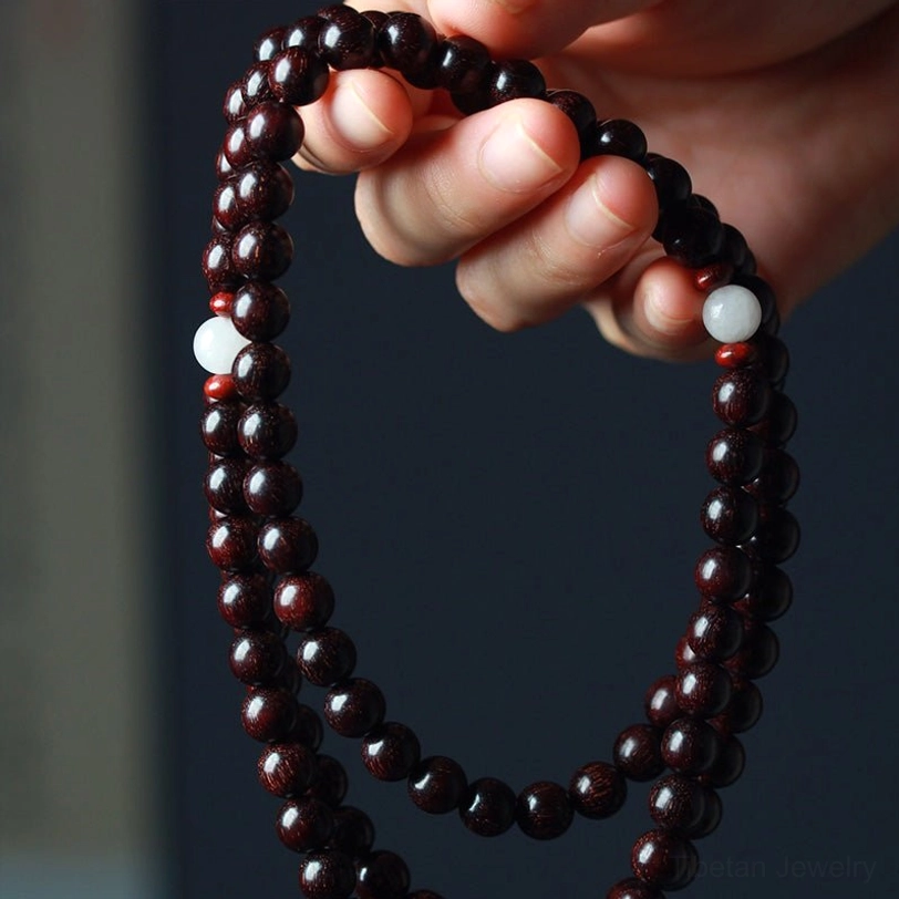 Single red sandalwood prayer bracelet held in hands showing bead size and white spacer accents