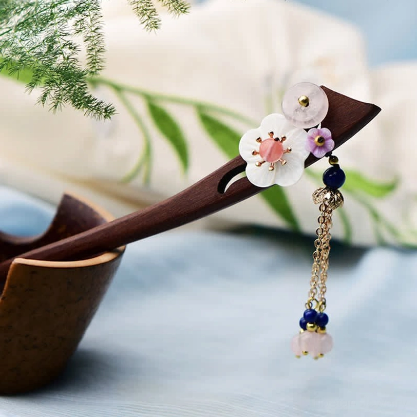 Curved red sandalwood hairpin with pink crystal flower and long single tassel on green foliage