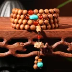 Sandalwood lotus mala bracelet with 108 beads and red turquoise lotus tassel on wooden display stand