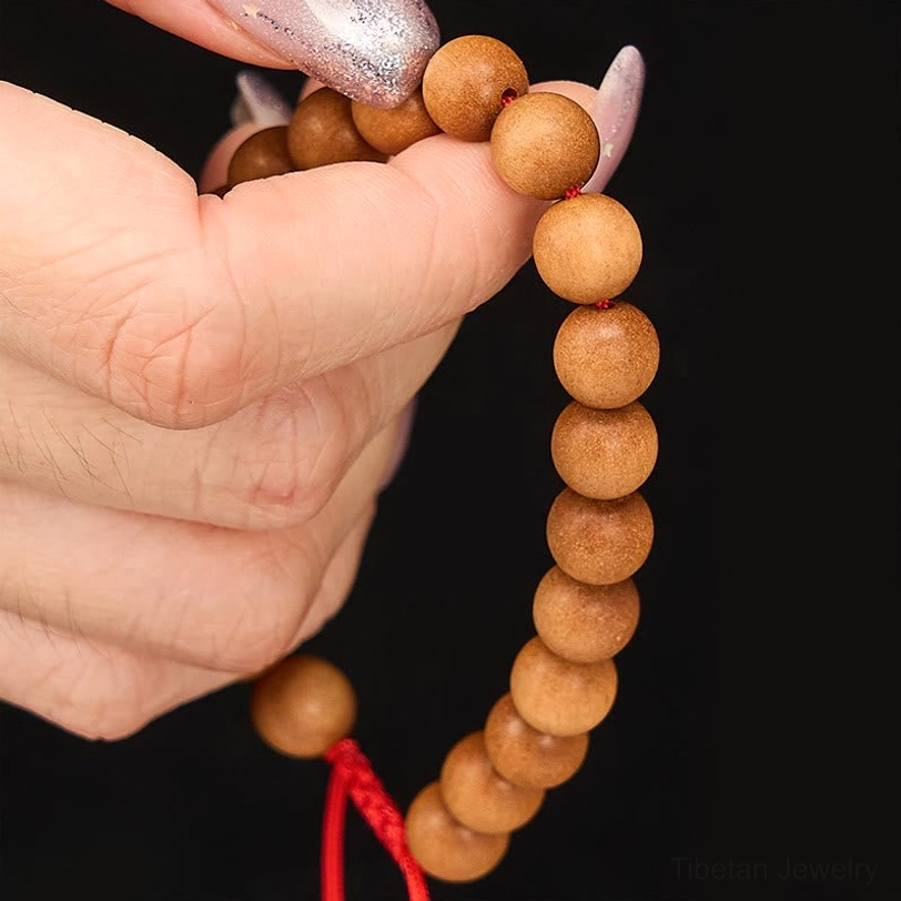 Detailed close-up of sandalwood beaded wrist mala showing individual bead strand, tan round beads with red bottom cord