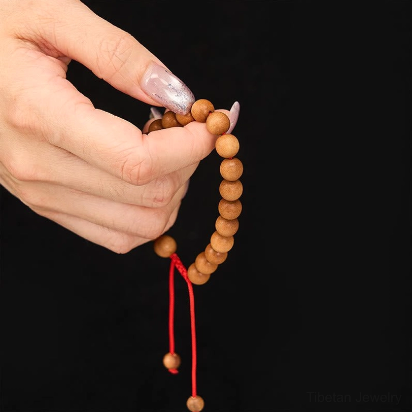 Close-up handheld view of sandalwood mala bracelet with visible natural wood grain texture, worn on manicured hands