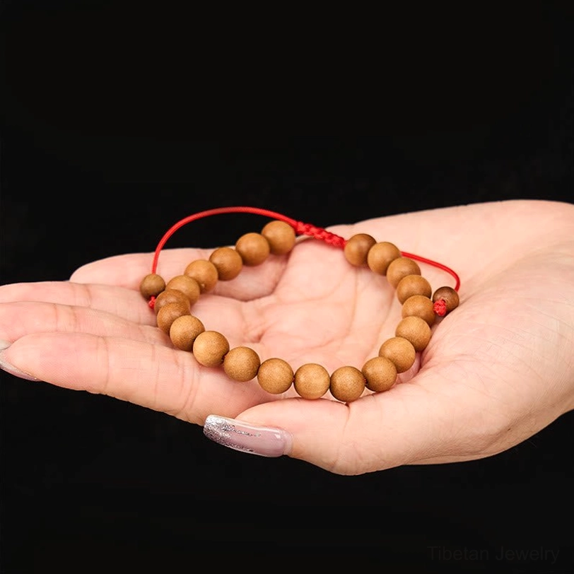 Sandalwood mala bracelet resting on person's palm, warm brown wooden beads with secure red protective cord