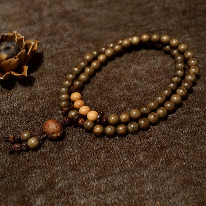 Single-loop sandalwood mala bracelet with mixed dark and light wooden beads on dark fabric background