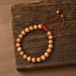 Natural sandalwood mala bracelet with 8mm beads and red adjustable cord displayed on dark wooden surface, top-down view