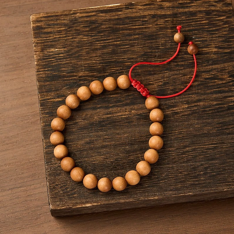 Natural sandalwood mala bracelet with 8mm beads and red adjustable cord displayed on dark wooden surface, top-down view