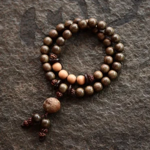Double-loop sandalwood mala bracelet with uniform round beads and knotted tassel charm on dark fabric