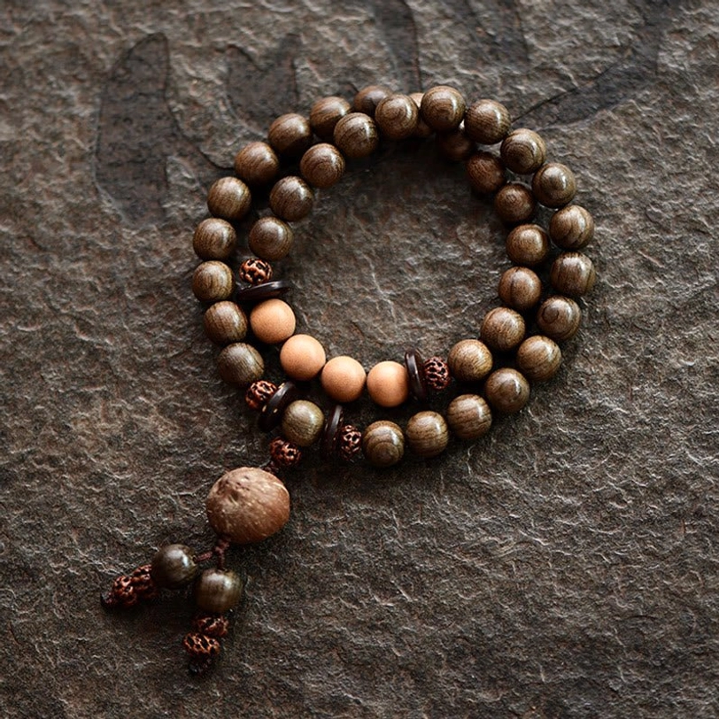 Double-loop sandalwood mala bracelet with uniform round beads and knotted tassel charm on dark fabric