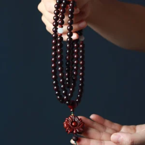 Close-up detail of red sandalwood prayer beads with white spacer beads and carved lotus pendant in hand