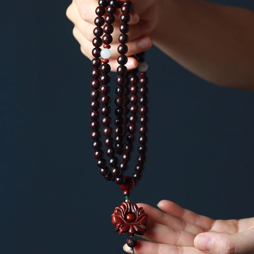 Close-up detail of red sandalwood prayer beads with white spacer beads and carved lotus pendant in hand