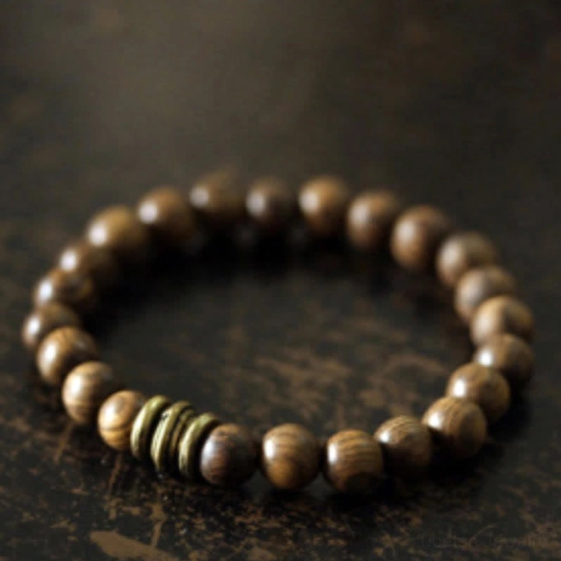 Close-up of sandalwood bracelet showing smooth brown wooden beads with natural grain texture, bronze metal accents, and premium elastic string