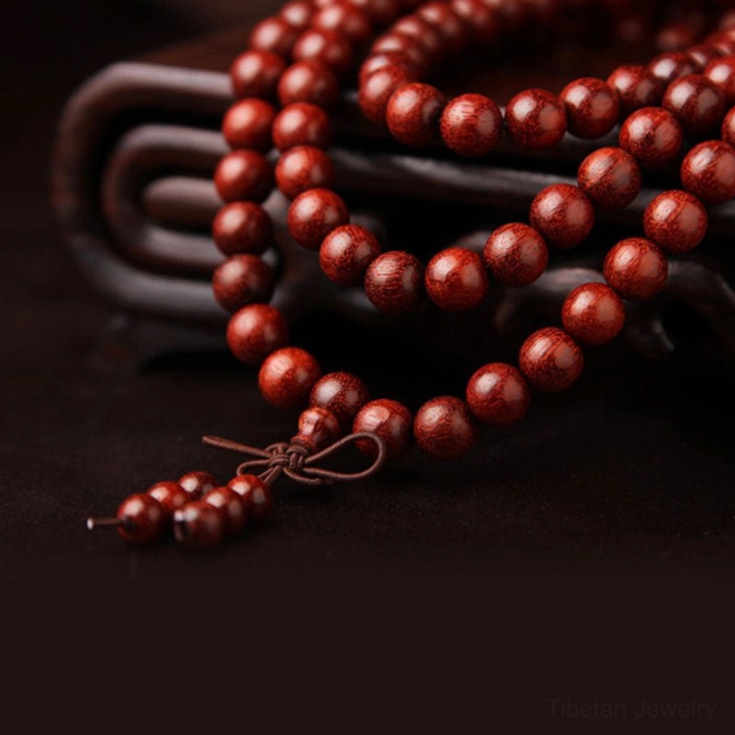 Loosely draped sandalwood prayer beads with visible wood grain detail, displayed on dark curved base showing reddish-brown bead texture
