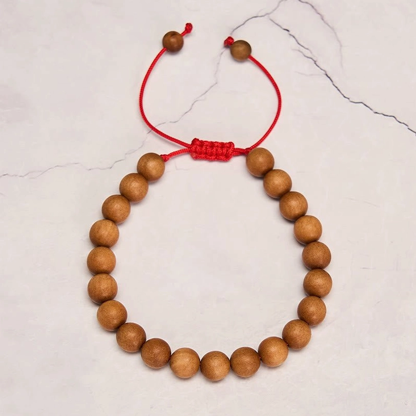 Sandalwood grounding mala bracelet on marble surface, featuring round wooden beads and red woven knot cord