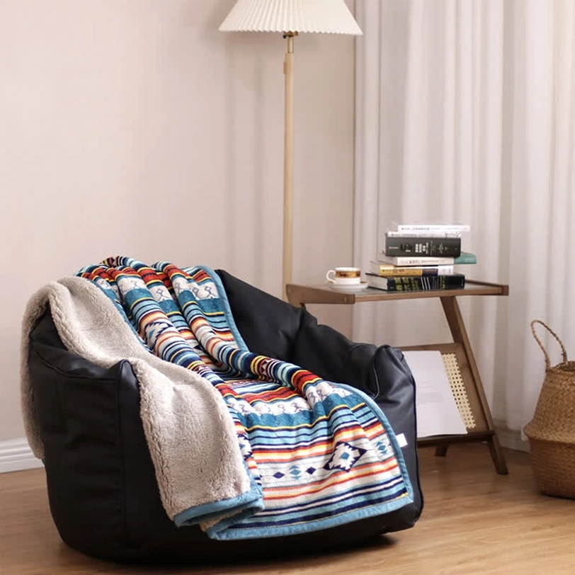 Reversible sherpa throw blanket with geometric ethnic pattern on cozy bean bag, showing fuzzy fleece backing and bohemian design