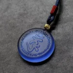 Shurangama Mantra Liuli crystal pendant necklace with frosted navy blue crystal, hand-engraved Sanskrit mantra, red woven cord accent, and gold spacer bead on dark leather background