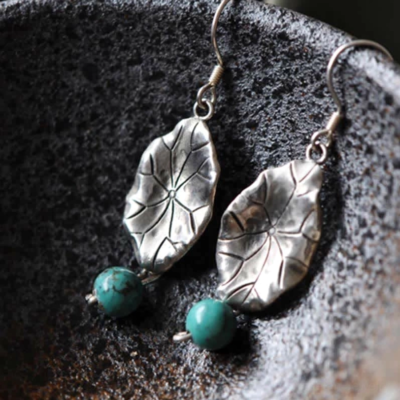 Detailed side view of sterling silver lotus leaf turquoise earrings on rough ceramic bowl surface