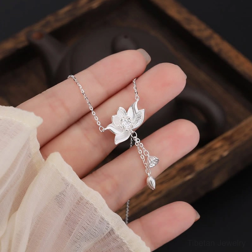Hand-held close-up of polished 999 silver lotus pendant showing fine details and delicate craftsmanship