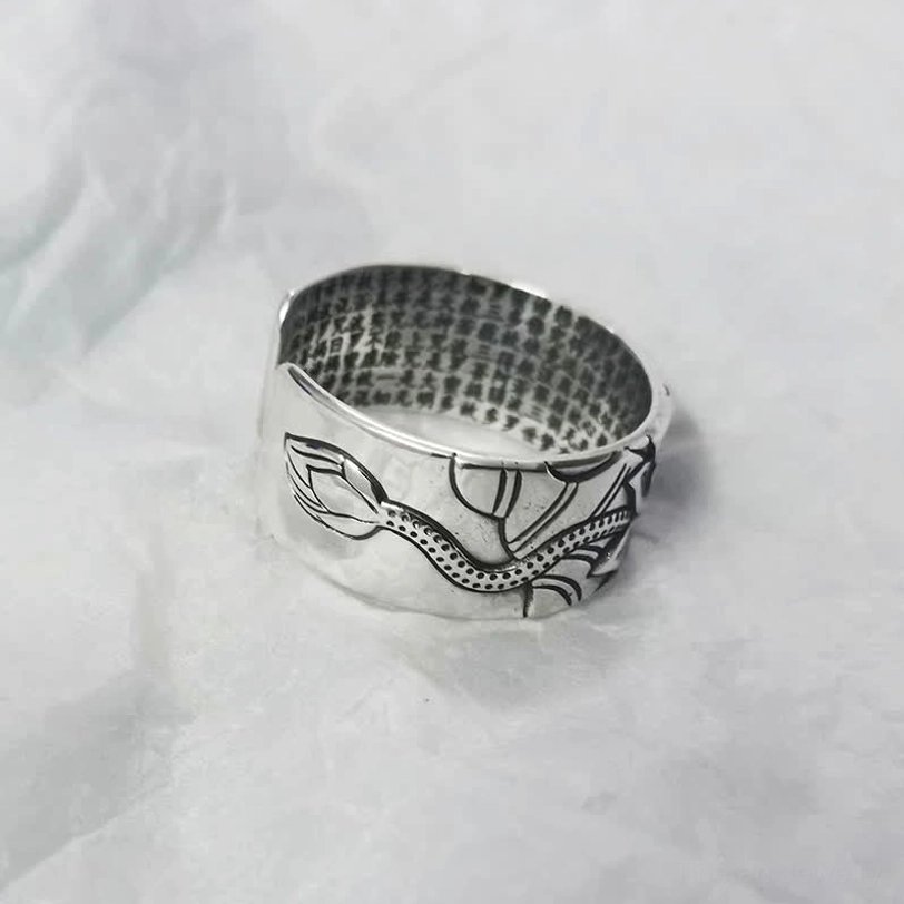 Hand-crafted 999 silver lotus heart sutra ring displaying embossed lotus stem and bud motif, side oblique view on white fabric