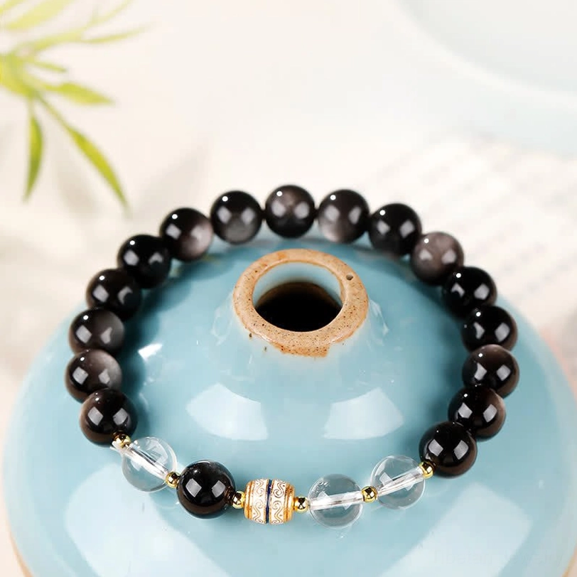 Silver Sheen Obsidian Nine-Eye Dzi Bead Protection Bracelet top-down view with clear quartz spacers and hand-painted Dzi bead