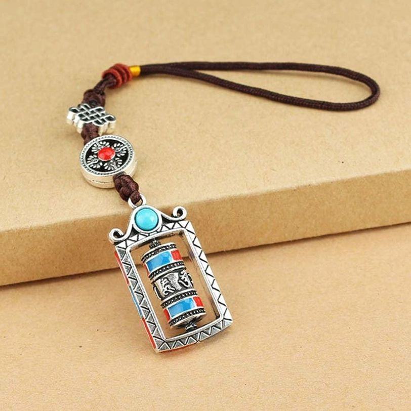 Flat lay Tibetan prayer wheel keychain on cardboard background, turquoise blue rotatable mechanism, silver alloy with adjustable dark brown lanyard