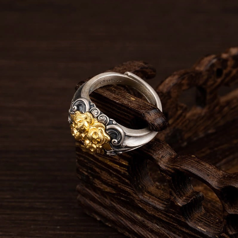 Side view of dual-tone Tibetan skull ring with gold front motif and curved silver band resting on carved wooden display base