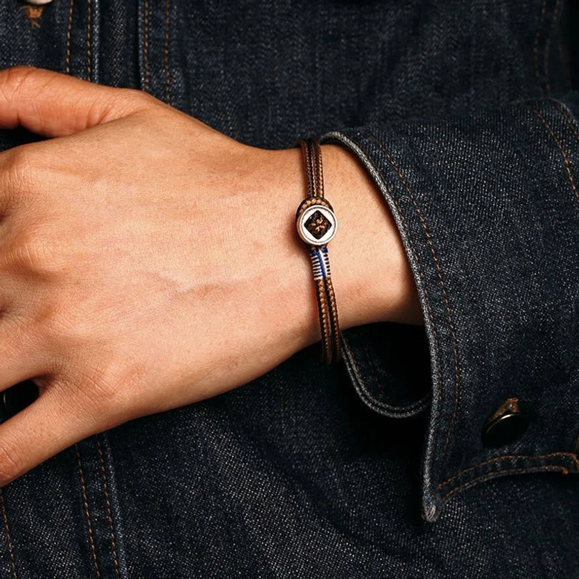 Side hand view of brown tibetan woven bracelet with silver decorative buckle worn with denim clothing