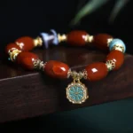 South Red Agate Bagua Dzi Bead Bracelet with blue enamel charm on dark wooden surface, showing authentic red agate beads and gold-toned metal accents