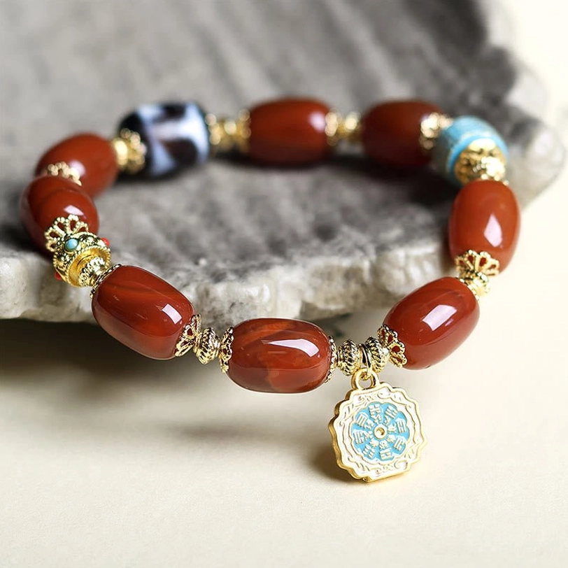 Side angle view of South Red Agate Bagua Dzi Bead Bracelet on gray stone mat, highlighting light blue Bagua pendant and gold metal details
