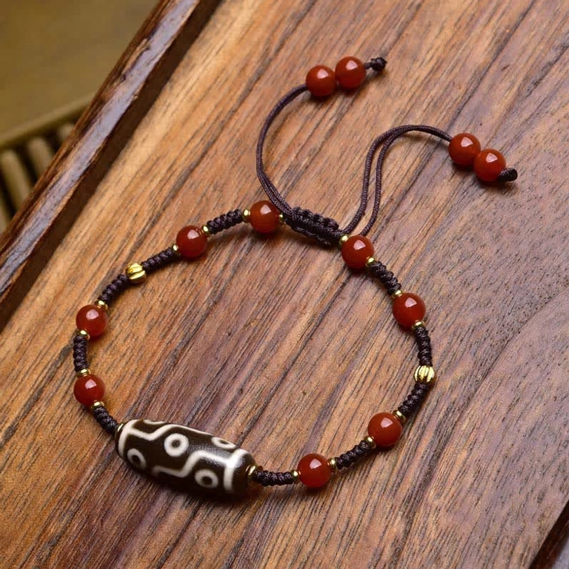 South Red Agate Dzi bead protection bracelet close-up flat lay showing red agate beads, metal spacers, and adjustable brown braided cord