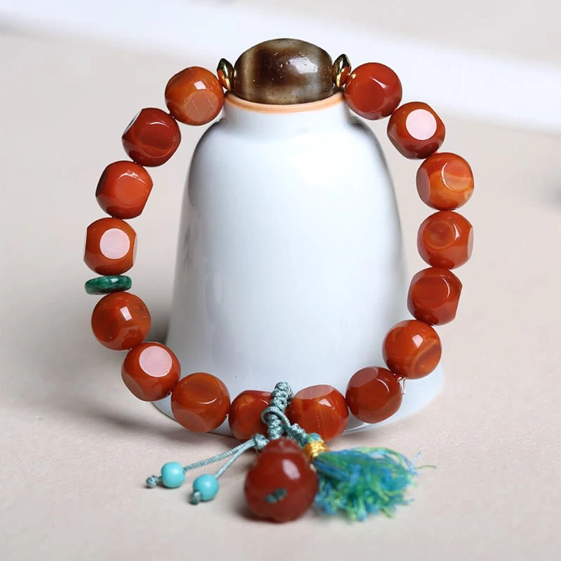 South Red Agate Pixiu Dzi Bracelet - High-Angle Top-Down Shot with Faceted Red Agate Beads, Brown Dzi Bead, and Turquoise Tassel on Porcelain Display Stand