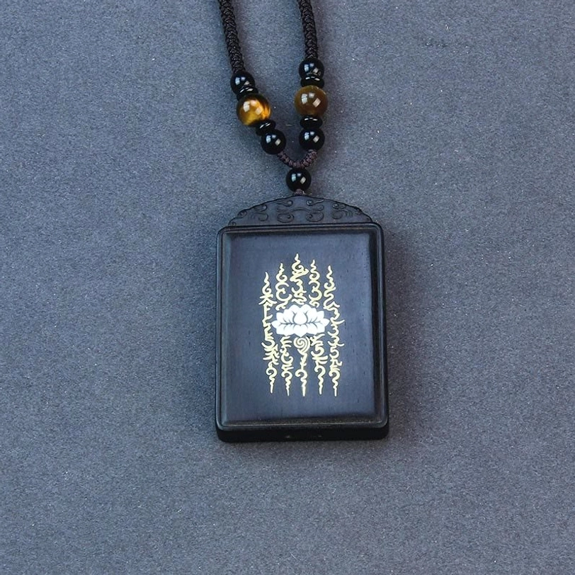 Square ebony lotus pendant hanging from beaded necklace, spiritual Tibetan jewelry against dark background