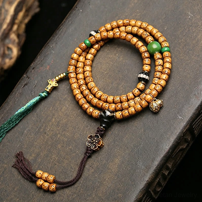 Overhead view of Star Moon Bodhi 108 mala on dark wooden table with tan spotted beads green tassel accent metal flower charm and dark braided cord