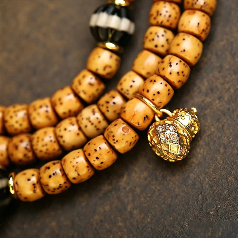 Side view close-up of Tibetan Star Moon Bodhi mala strand with tan spotted cylinder beads gold bell charm and striped spacer bead