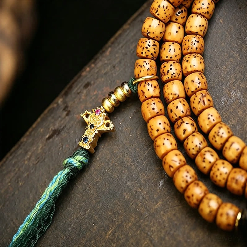 Close-up side view of Tibetan Star Moon Bodhi prayer mala with tan spotted beads green tassel cord and gold metal guru charm