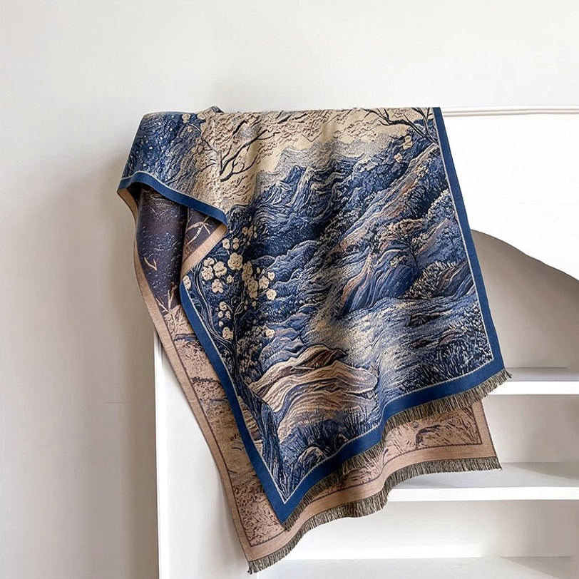 Steel blue Tibetan landscape scarf with navy mountain art pattern folded on white shelf, angled front view with visible frayed hem