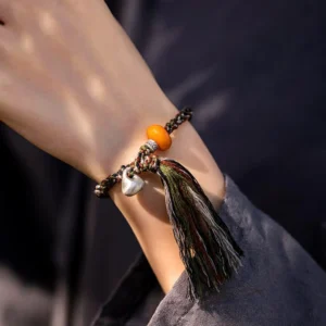 Close-up side view of protection bracelet worn on wrist showing amber bead, teardrop silver steelyard charm, and braided cord detail