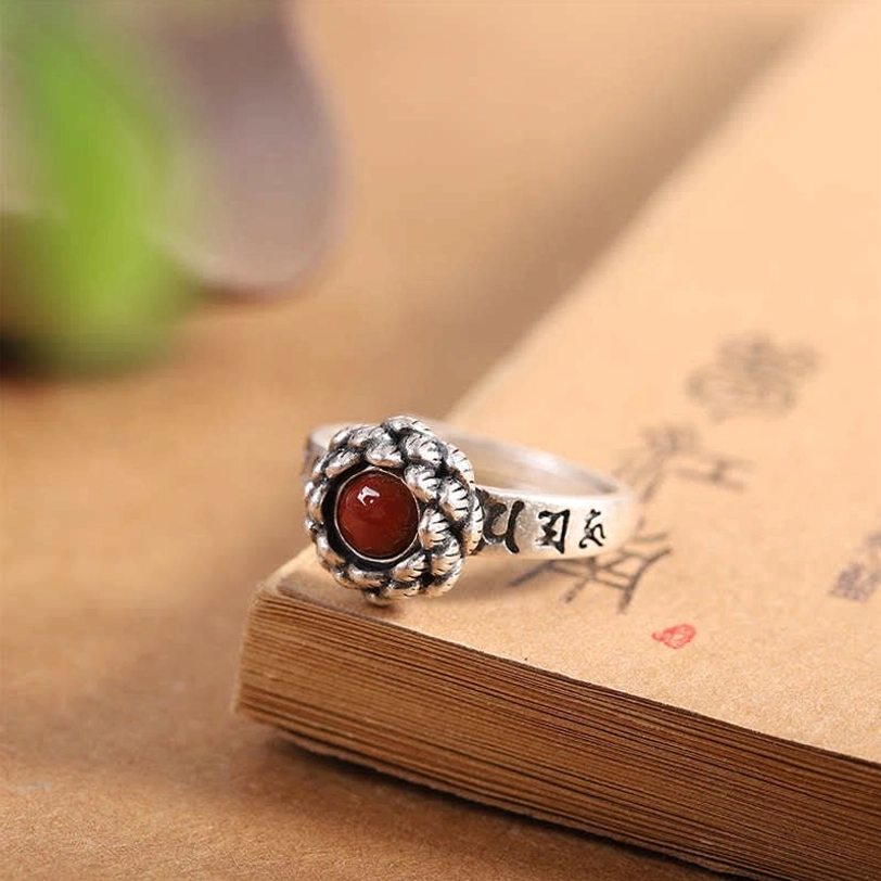 Handcrafted sterling silver lotus red agate confidence ring, top-side angle on vintage book