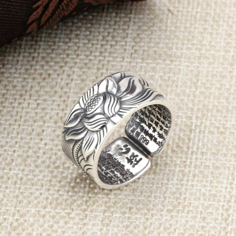 Handmade 999 sterling silver lotus heart sutra protection ring featuring full lotus carving with purity mark inside, oblique top view on dark fabric