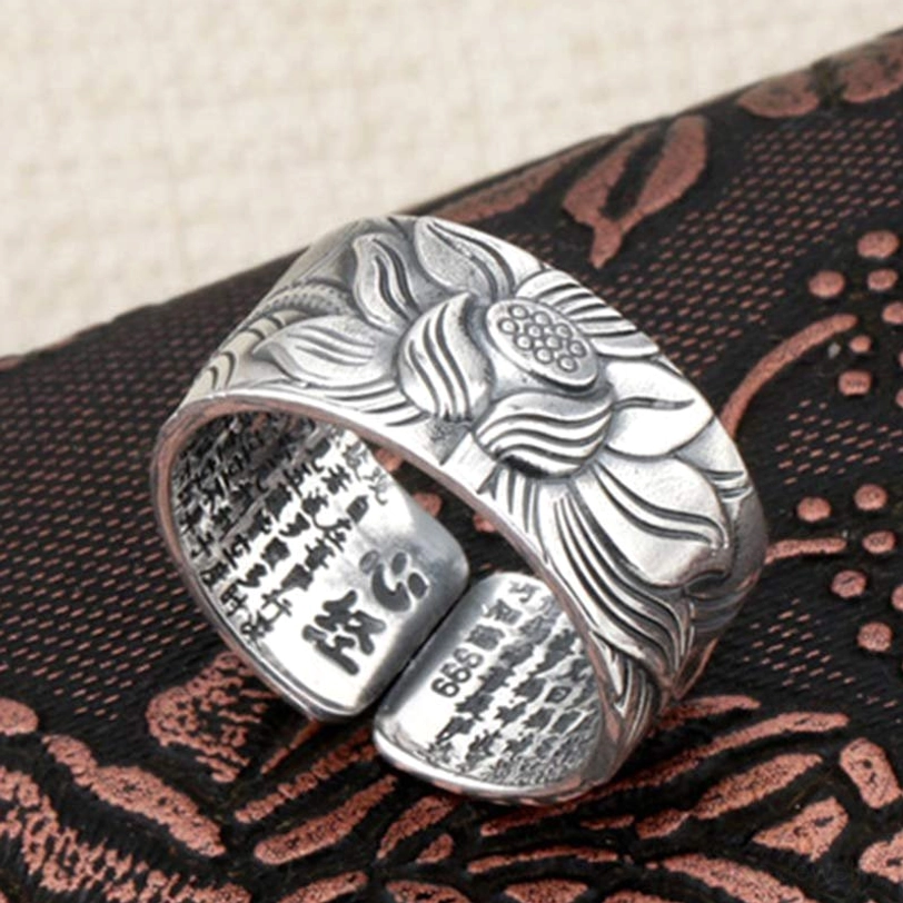 Adjustable silver lotus heart sutra ring displaying purity mark and sutra text on inner band, side oblique view on embroidered fabric