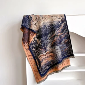 Teal Tibetan wrap scarf with mountain and blossom jacquard pattern folded on white shelf, overhead view showing contrasting border detail