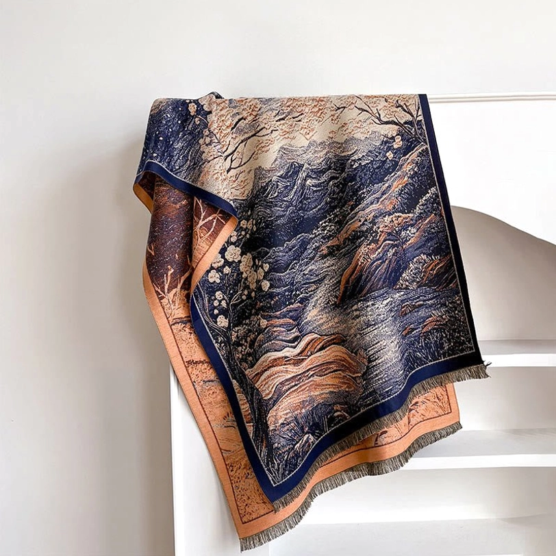 Teal Tibetan wrap scarf with mountain and blossom jacquard pattern folded on white shelf, overhead view showing contrasting border detail