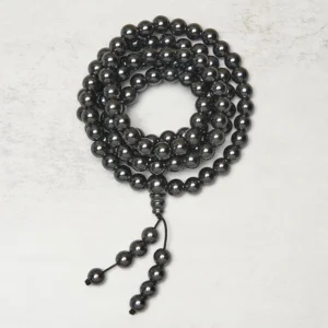 Circular terahertz prayer mala loosely coiled with hanging tassel on light grey background