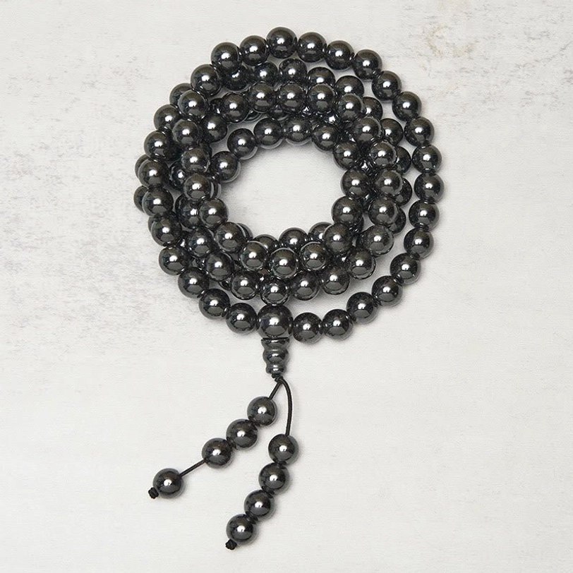 Circular terahertz prayer mala loosely coiled with hanging tassel on light grey background