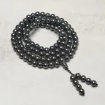 108 terahertz mala beads coiled flat lay with metallic dark beads and tassel pendant on grey tabletop