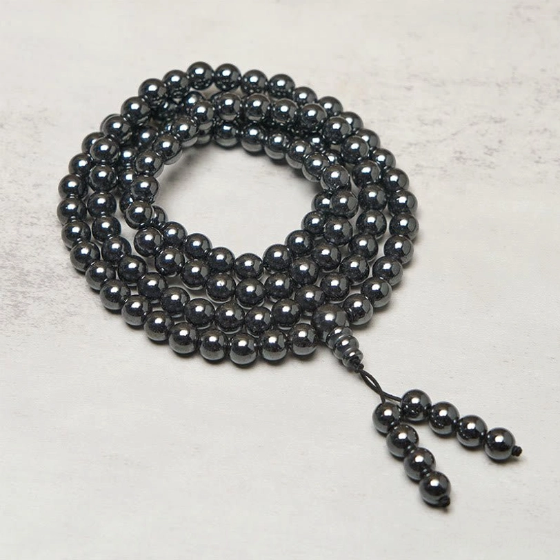108 terahertz mala beads coiled flat lay with metallic dark beads and tassel pendant on grey tabletop