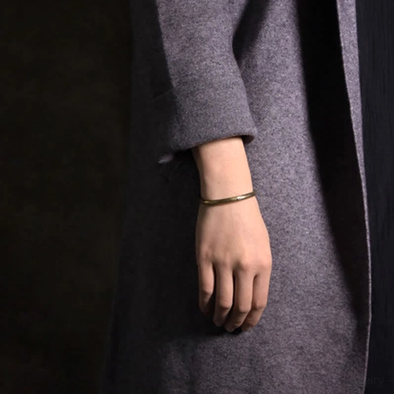 Slim open copper cuff bracelet worn on wrist with grey overcoat, minimalist styling