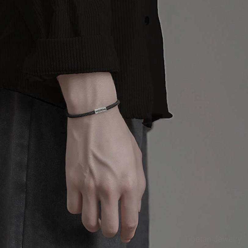 Tiny accent black braided bracelet with small silver bead worn on dark shirt showing slim band profile