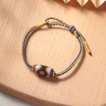 Tibetan three-eye Dzi bead bracelet in blue and gold, flat lay view showing complete adjustable design with sliding knot mechanism